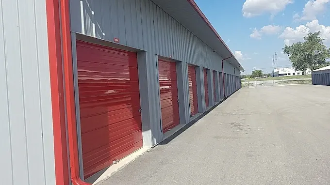 Outdoor storage units with red roll-up doors and paved vehicle access